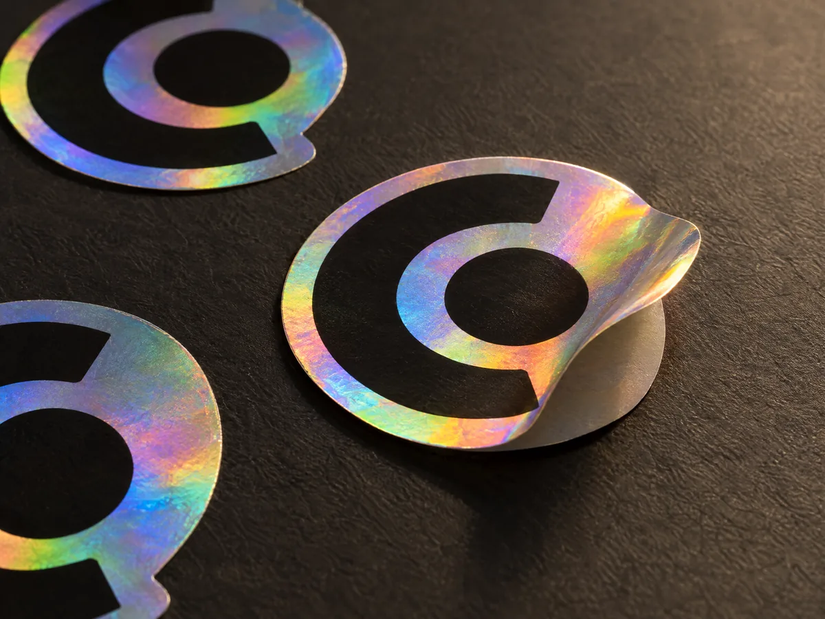 Holographic stickers with rainbow color shift and a dark circular design on a dark surface.